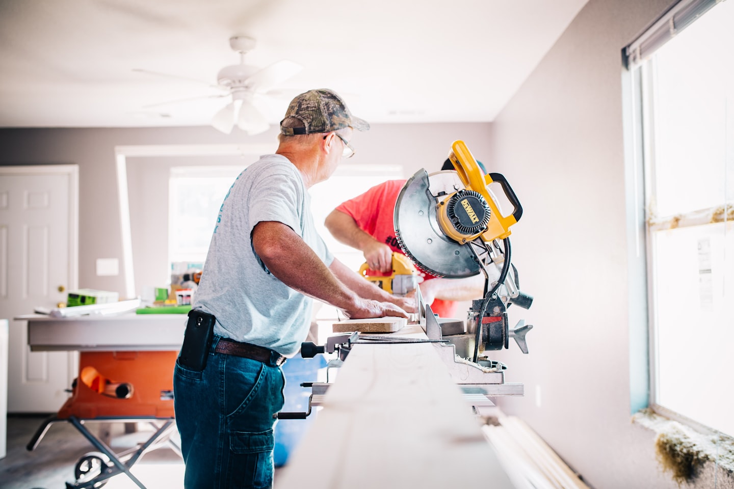 Two men working with saws on wood in a room under renovation.