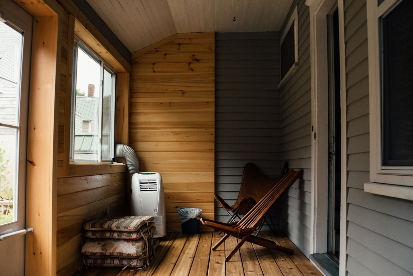Cozy sunroom with wooden walls, portable AC, and lounge chairs.